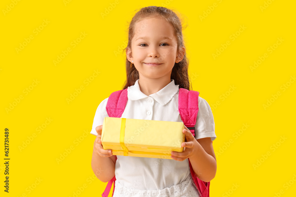 Little schoolgirl with gift on yellow background