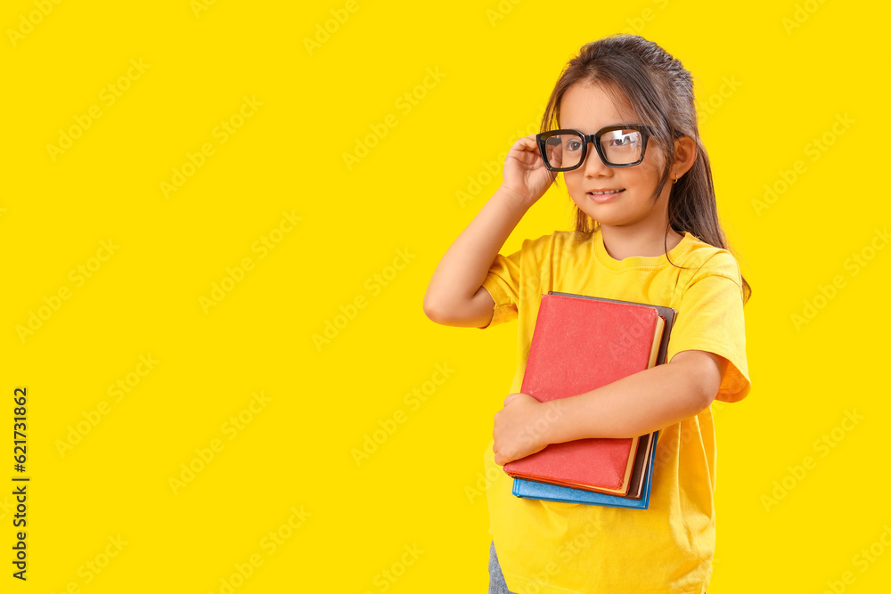 Little schoolgirl with books on yellow background