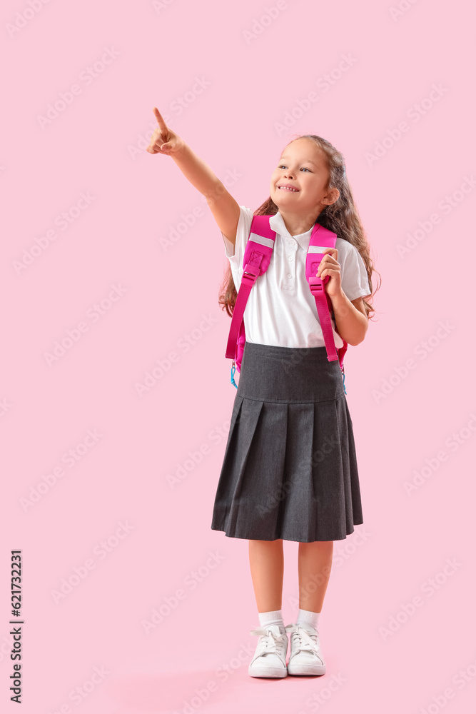 Little schoolgirl with backpack pointing at something on pink background