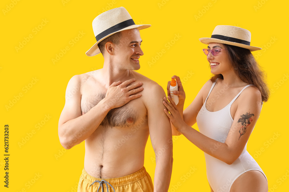 Young couple applying sunscreen cream on yellow background