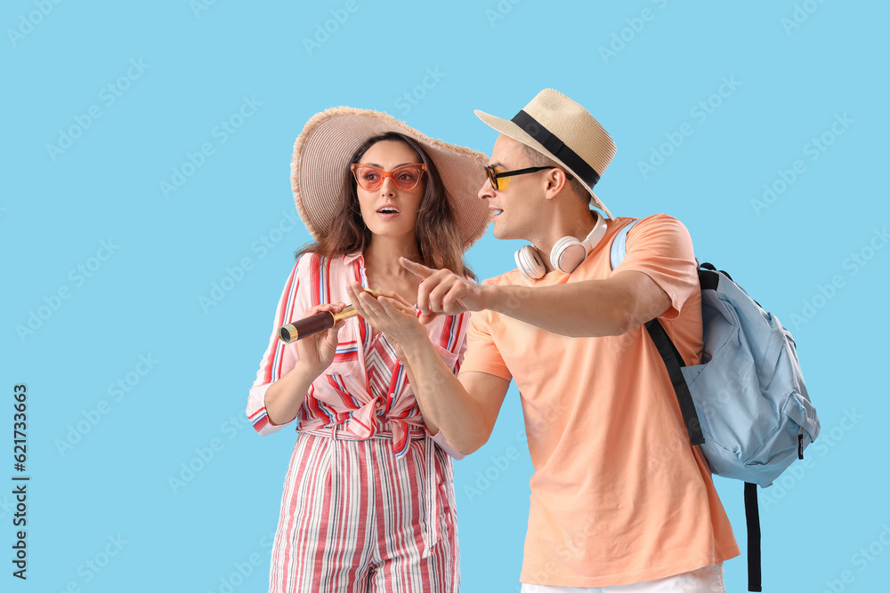 Young couple with spyglass and compass on blue background