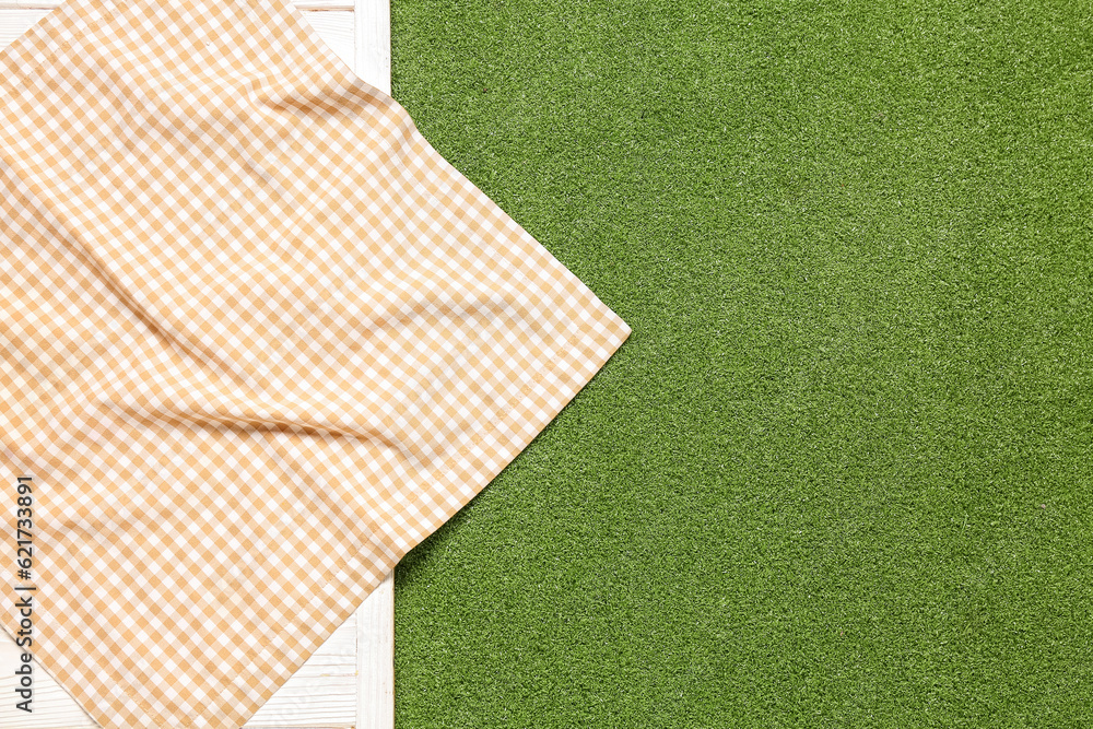 Clean napkin on light wooden table against green grass background