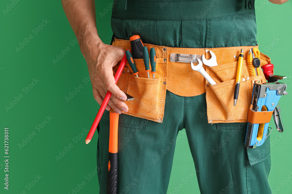 Mature builder with tool belt on green background, closeup