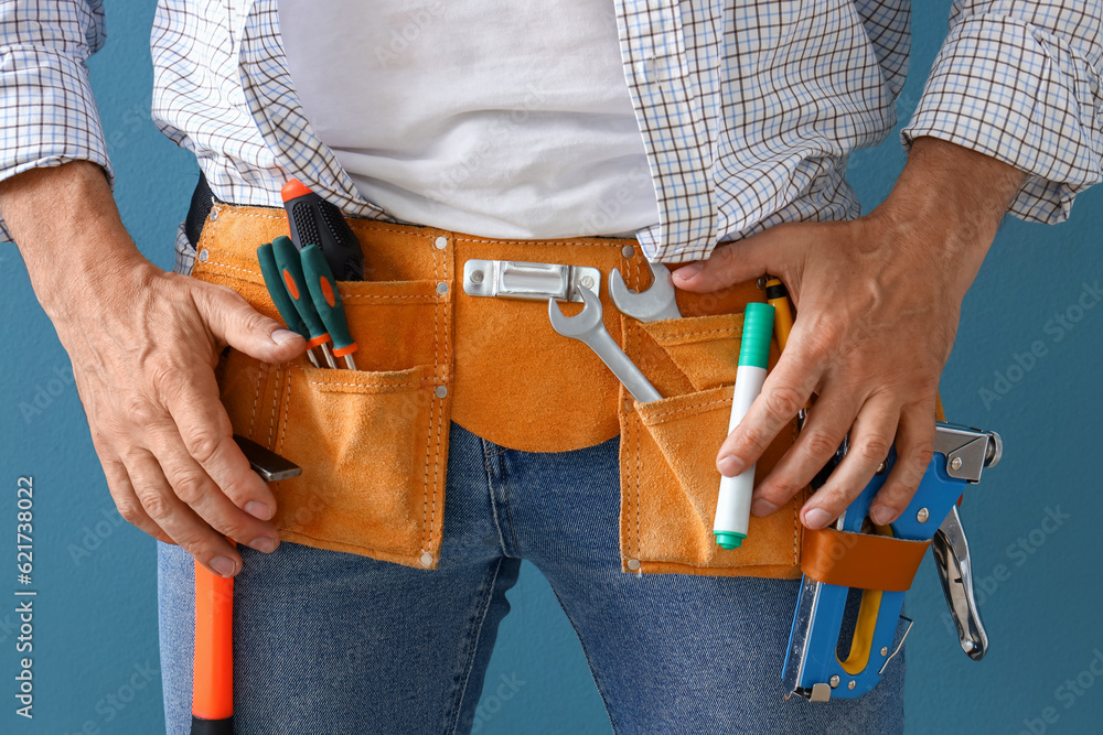 Mature builder with tool belt on blue background, closeup