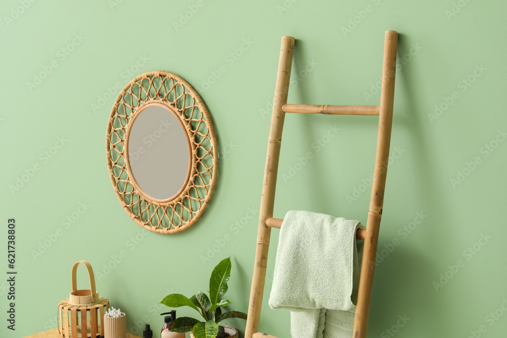 Wooden ladder with towel and mirror hanging on green wall in room