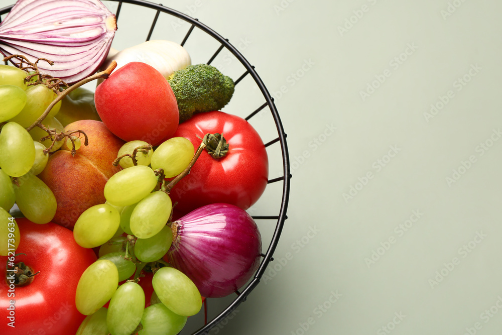 Basket with different fresh fruits and vegetables on green background, closeup