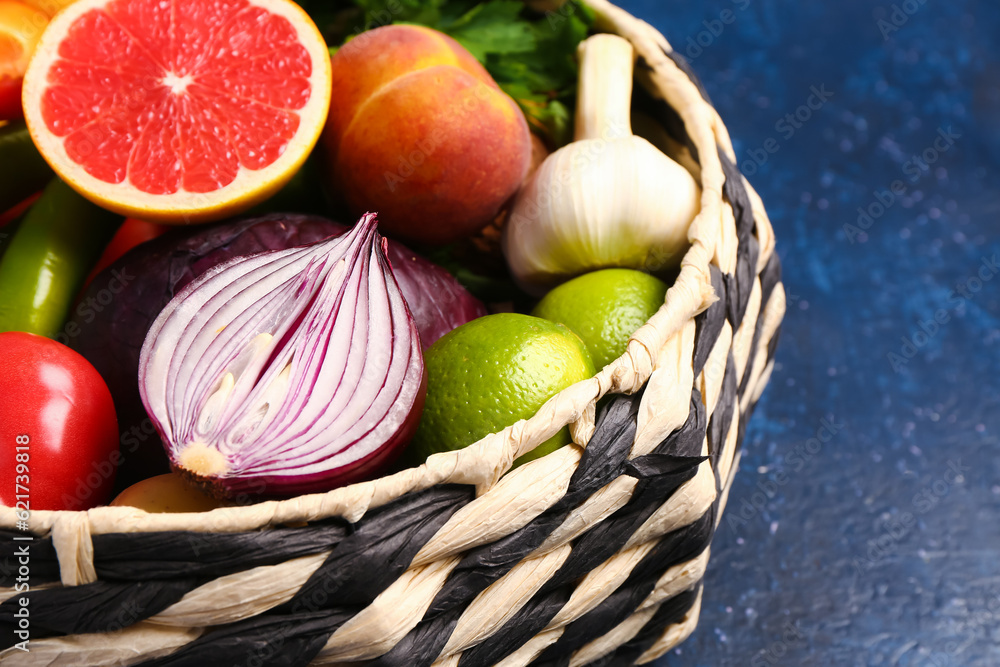 Wicker bowl with different fresh fruits and vegetables on blue background, closeup