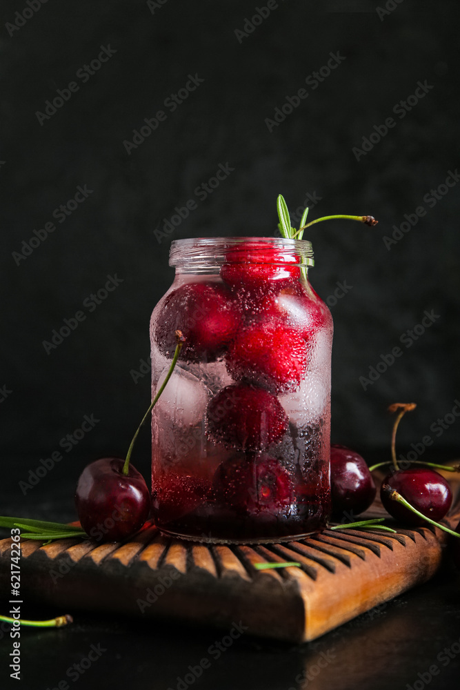 Wooden board with jar of tasty cherry lemonade and rosemary on black background