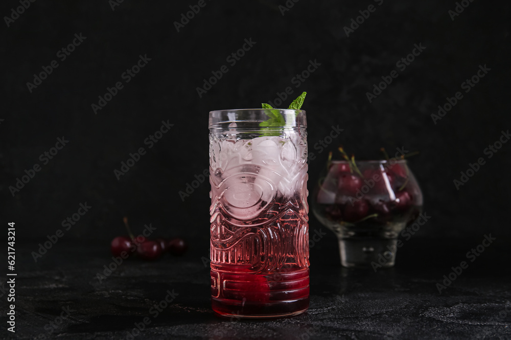 Glass of tasty cherry lemonade with mint on black background