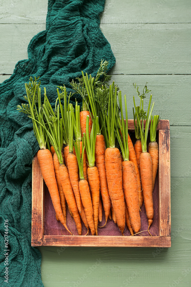 Box with fresh carrots on green wooden background