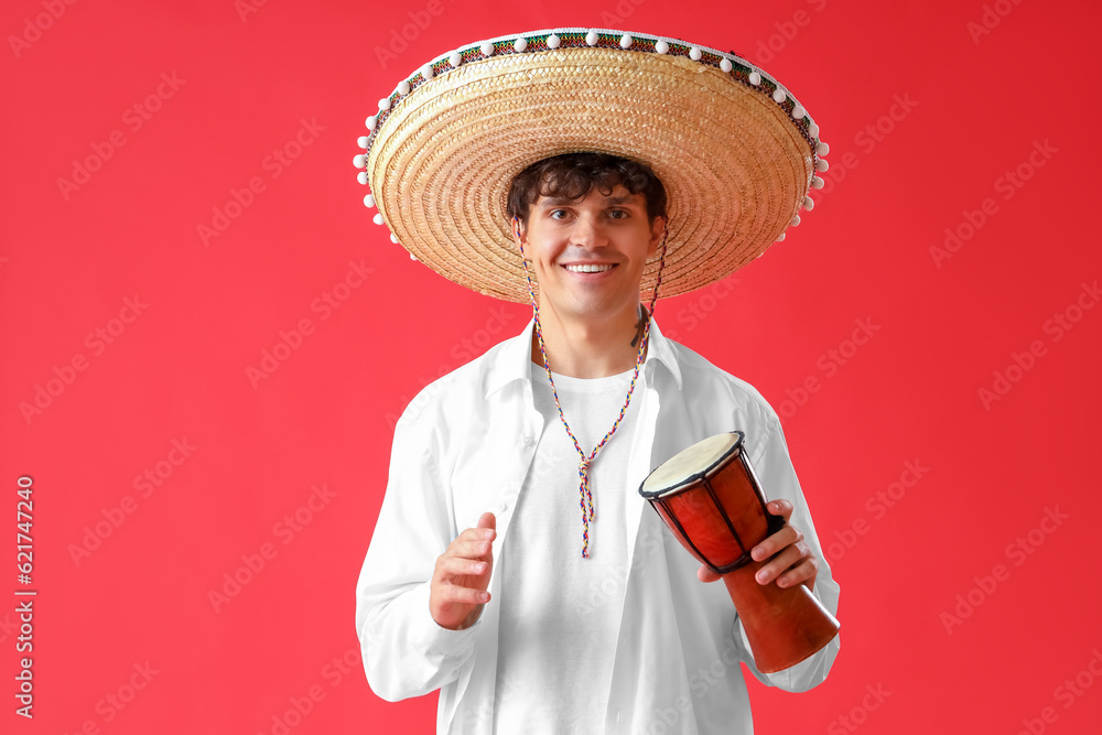 Young man in sombrero hat with drum on red background