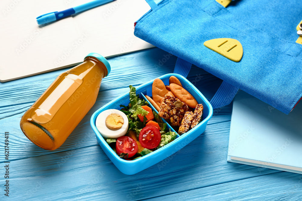 Backpack, stationery and lunchbox with tasty food on blue wooden background