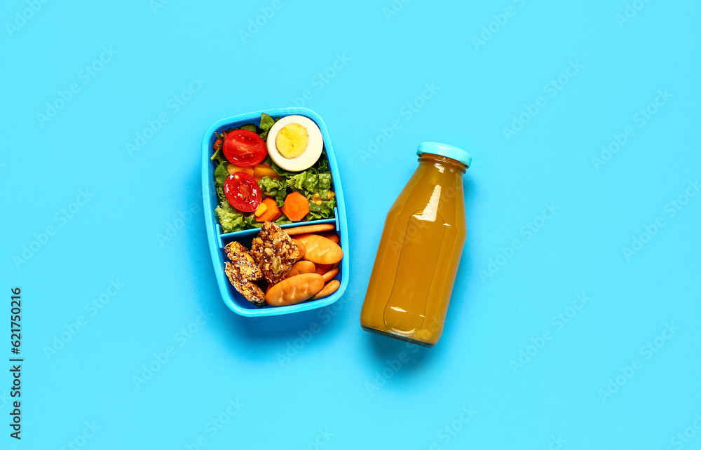 Bottle of juice and lunchbox with tasty food on blue background