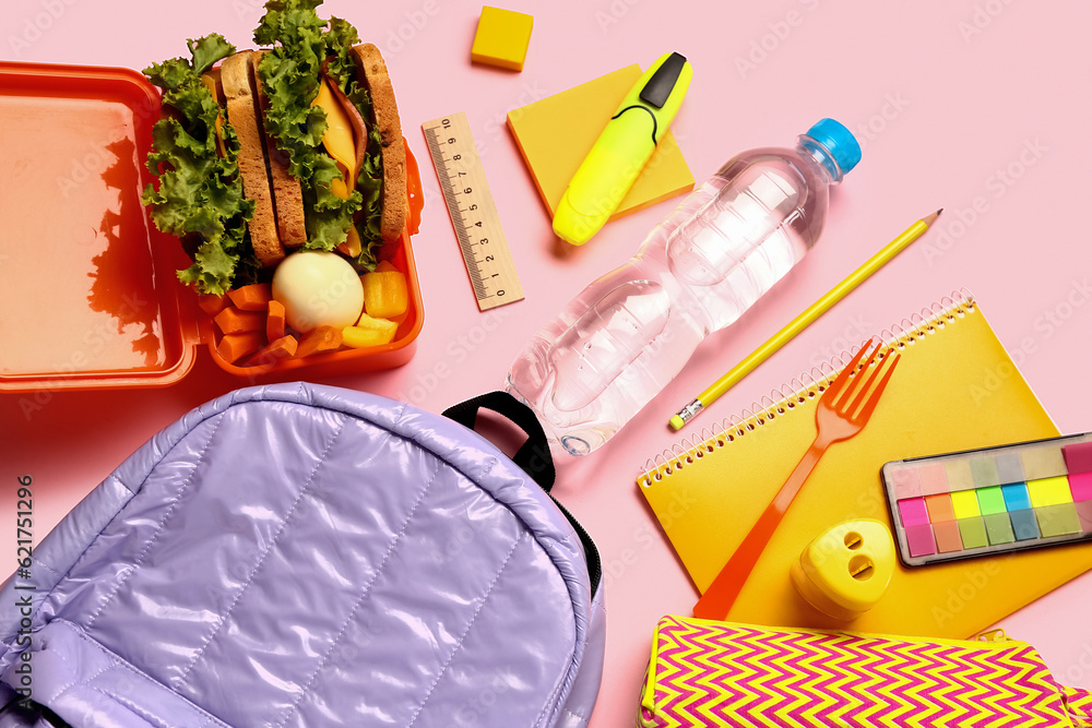 Backpack, stationery, bottle of water and lunchbox with tasty food on pink background