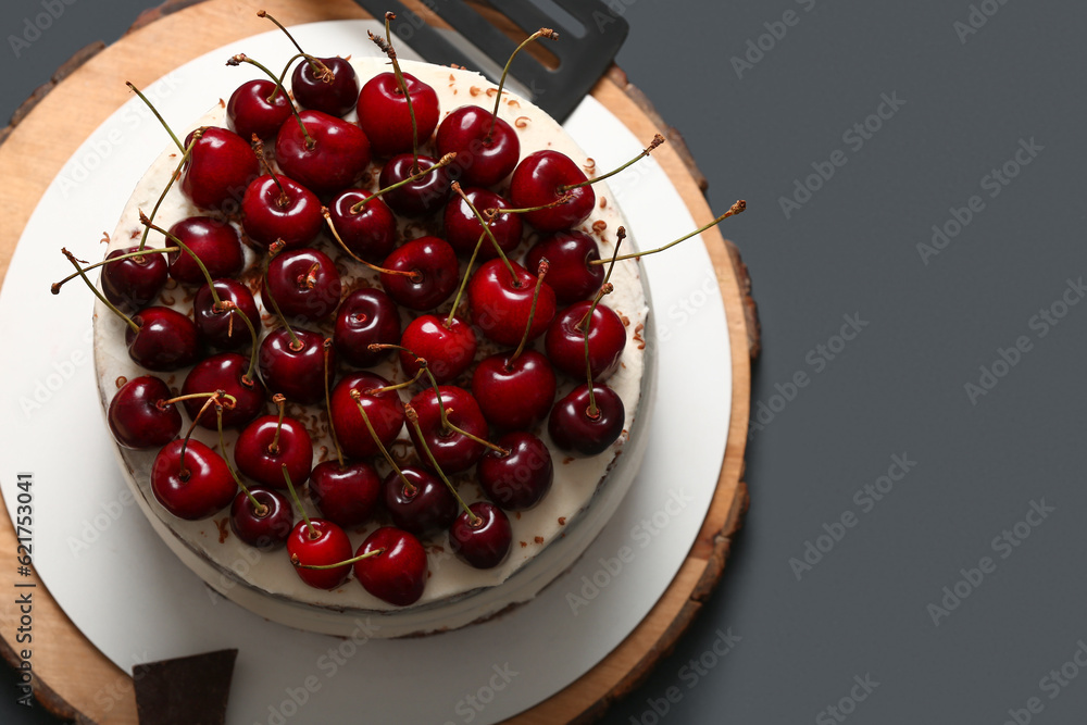 Wooden board with tasty cherry cake on dark background