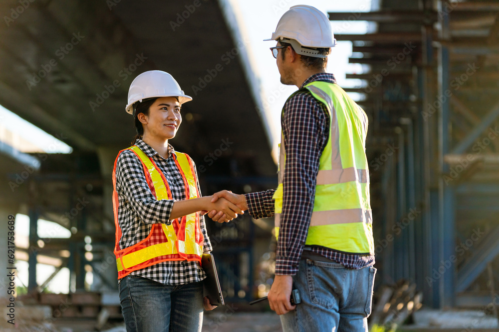 Asian women architect or construction workers in protective helmets and vests are shaking hands with