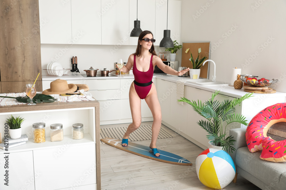 Young woman with wine and surfboard ready for summer vacation in kitchen