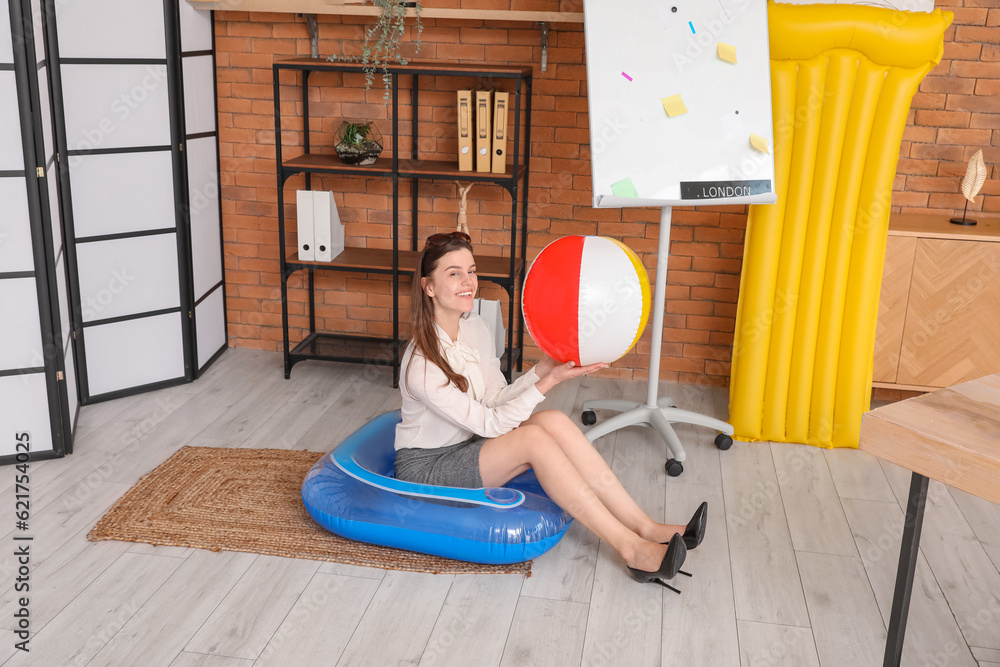 Young businesswoman with beach ball ready for summer vacation in office