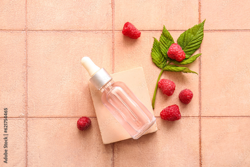 Decorative podium with bottle of cosmetic raspberry oil on pink tile background