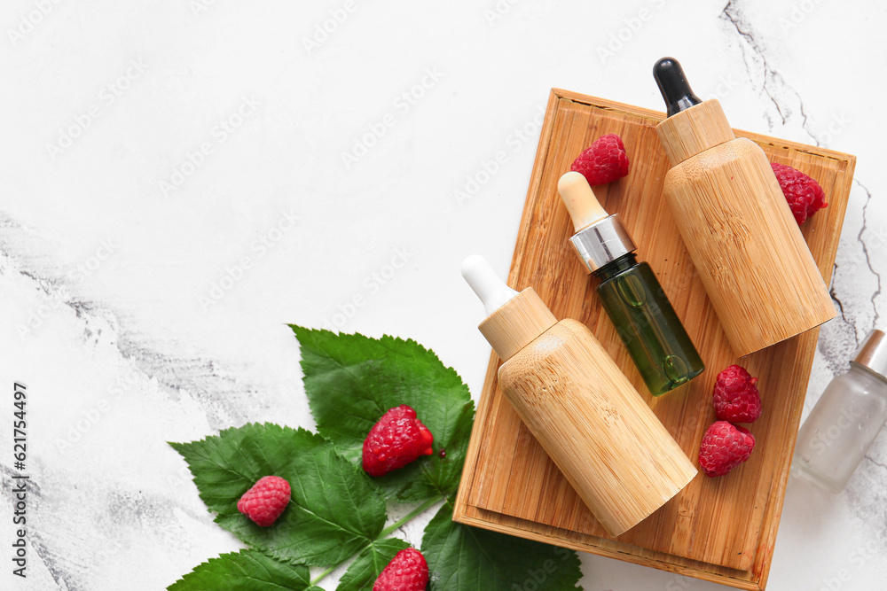 Wooden podium with bottles of cosmetic raspberry oil on white background