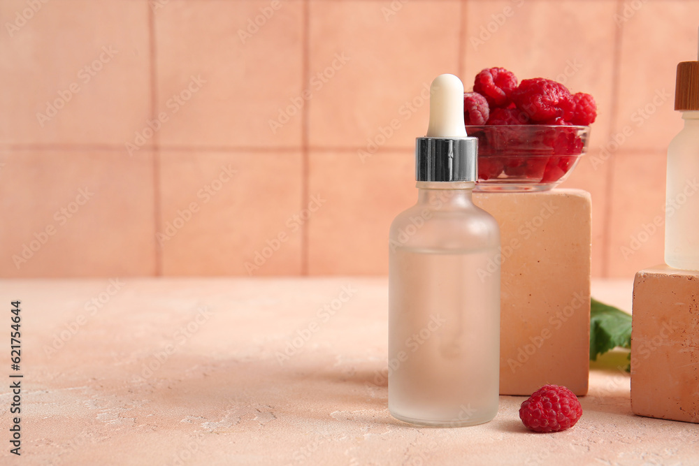 Decorative podium with bottle of cosmetic raspberry oil on pink table