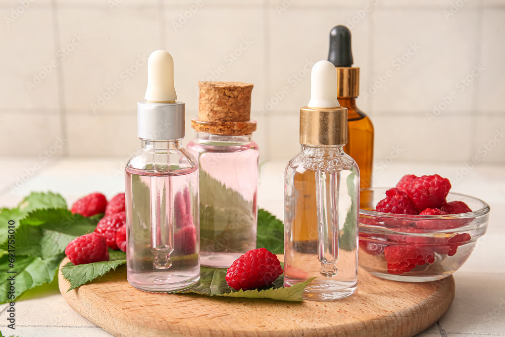 Wooden board with bottles of cosmetic raspberry oil on white tile background