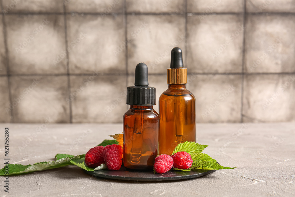 Board with bottles of cosmetic raspberry oil on grey table