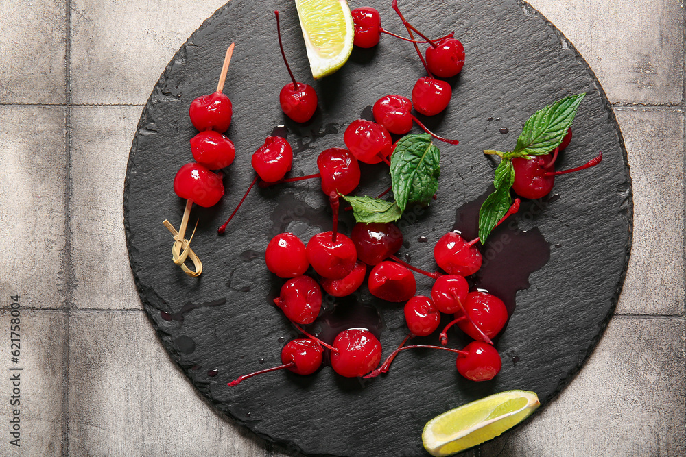 Slate board with tasty maraschino cherries on grey tile background