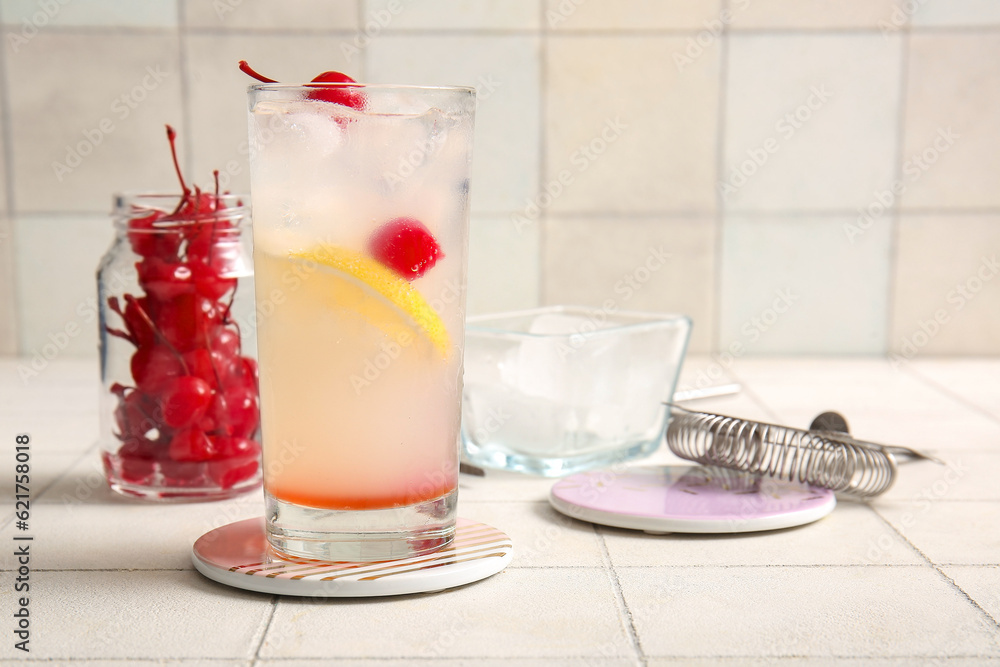 Glass of tasty cocktail with maraschino cherry on white tile background