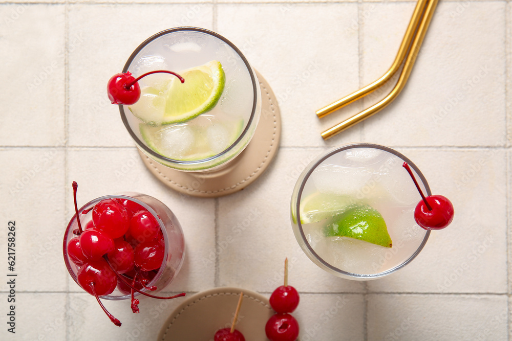 Glasses of tasty cocktail with maraschino cherries on white tile background