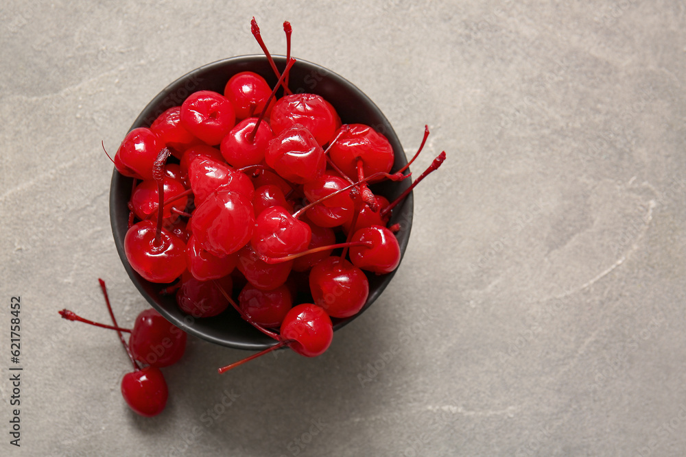 Bowl of tasty maraschino cherries on grey background