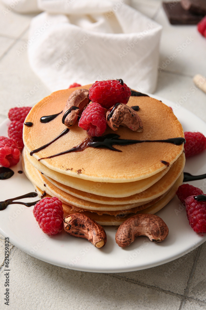 Plate of tasty pancakes with raspberries and nuts on white tile background