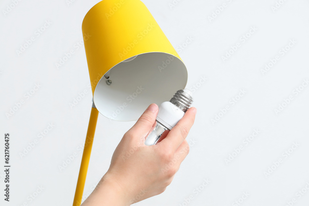 Woman changing light bulb in lamp on light background, closeup