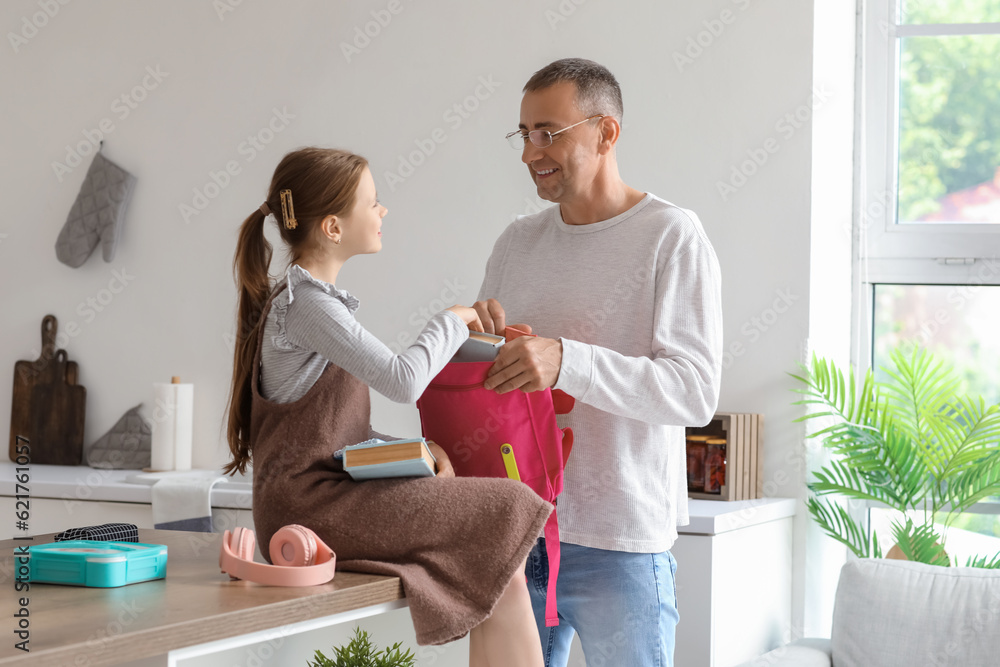 Father helping his little daughter to pack schoolbag in kitchen