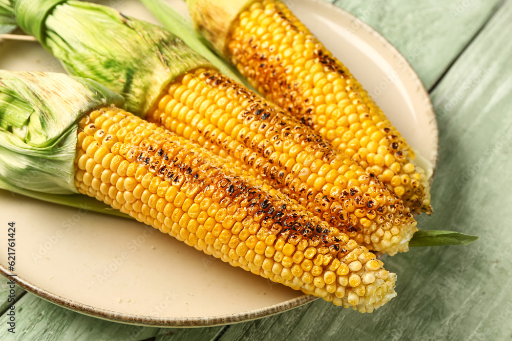 Plate with tasty grilled corn cobs on green wooden background