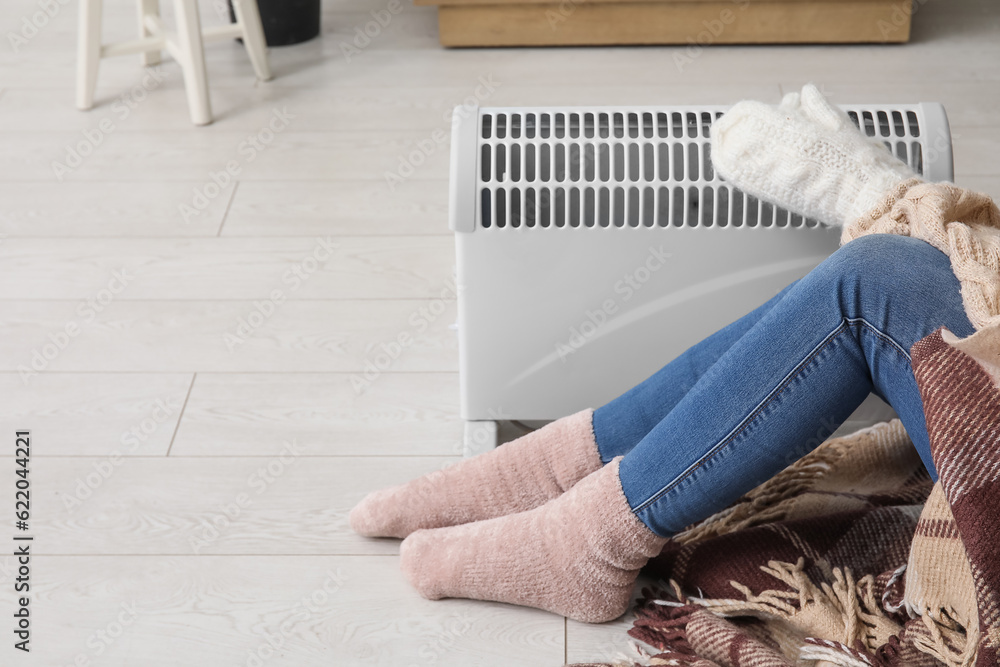 Woman in winter clothes warming near radiator at home, closeup