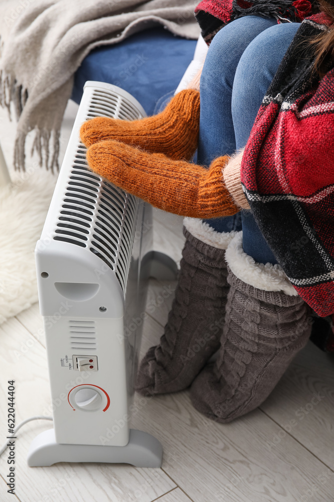 Woman warming hands in mittens near radiator at home, closeup