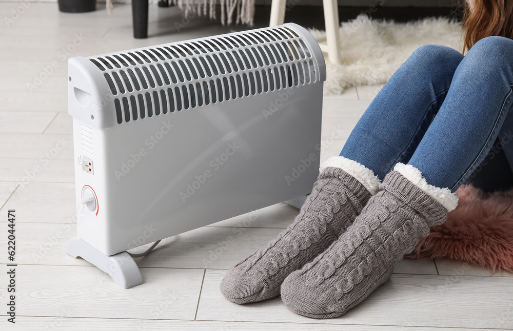 Woman in socks warming near radiator at home, closeup