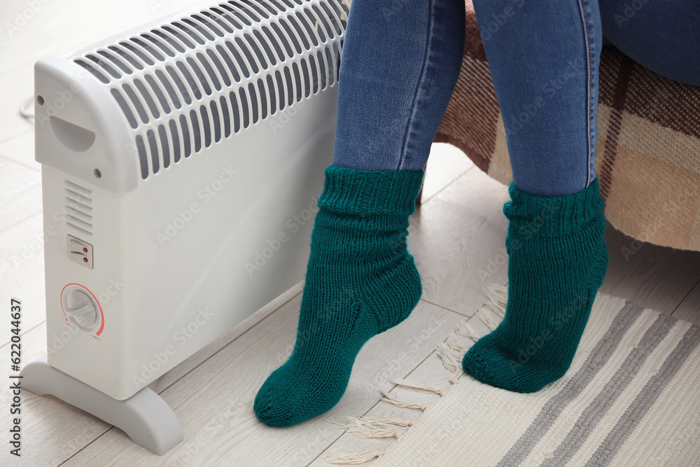 Woman in socks warming near radiator at home, closeup