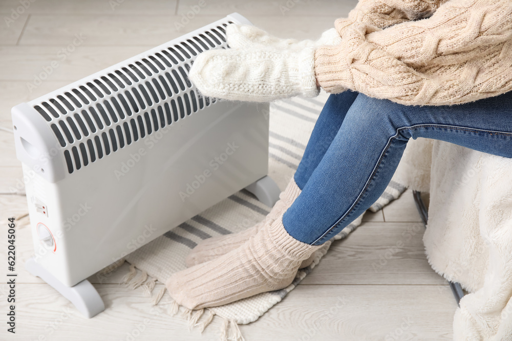 Woman warming hands in mittens near radiator at home, closeup