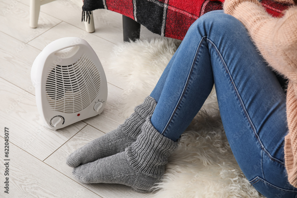 Woman warming legs in socks near radiator at home, closeup