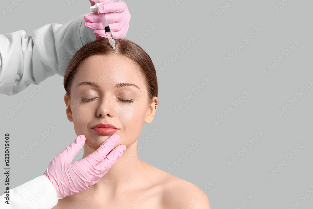 Young woman receiving filler injection in face against grey background