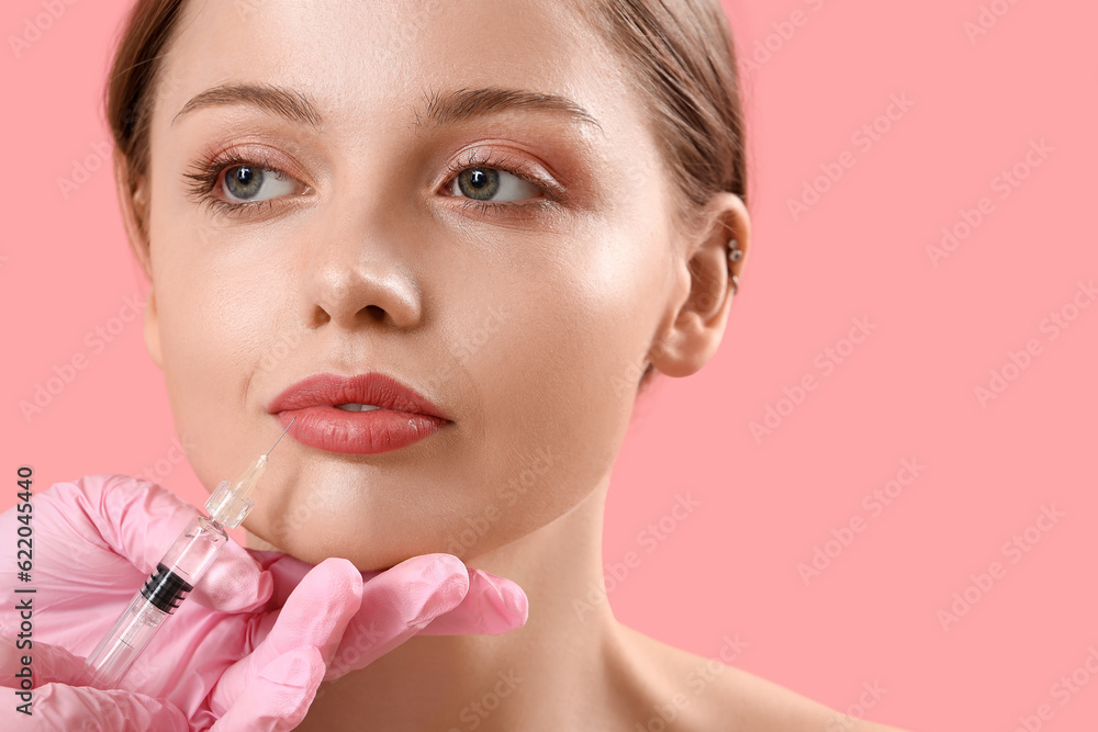 Young woman receiving filler injection in face against pink background