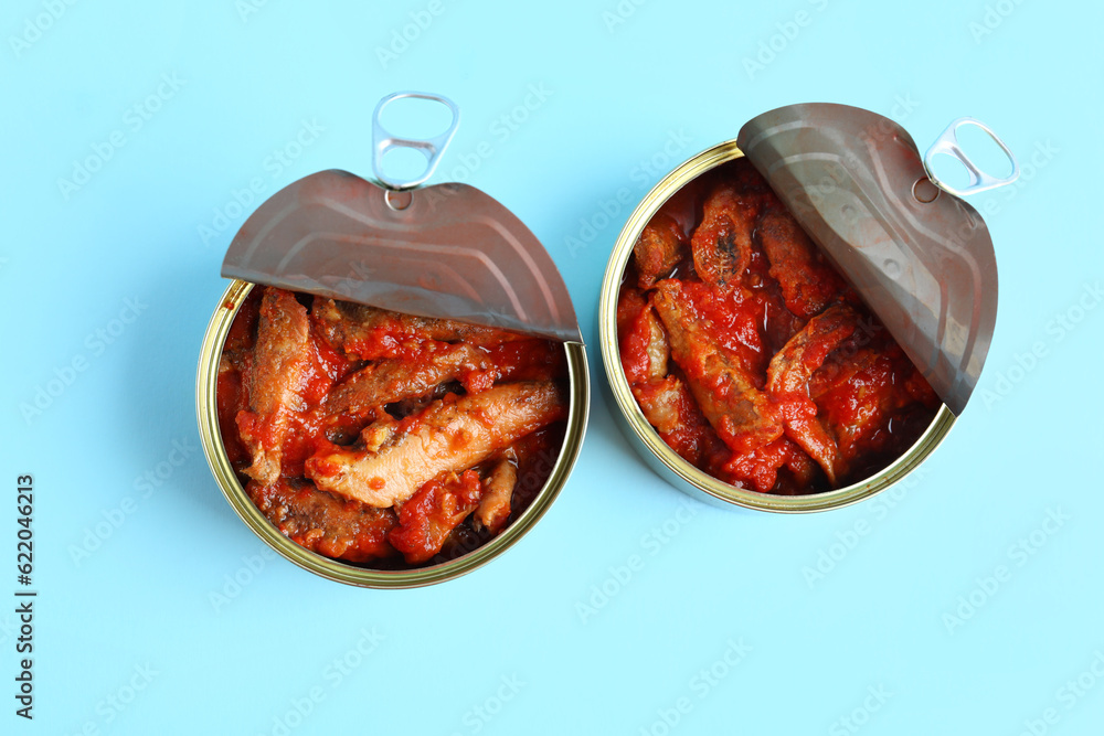 Opened tin cans with fish in tomato sauce on blue background