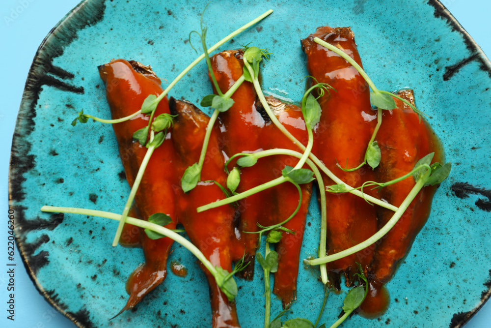 Plate with canned fish in tomato sauce and microgreens on blue background