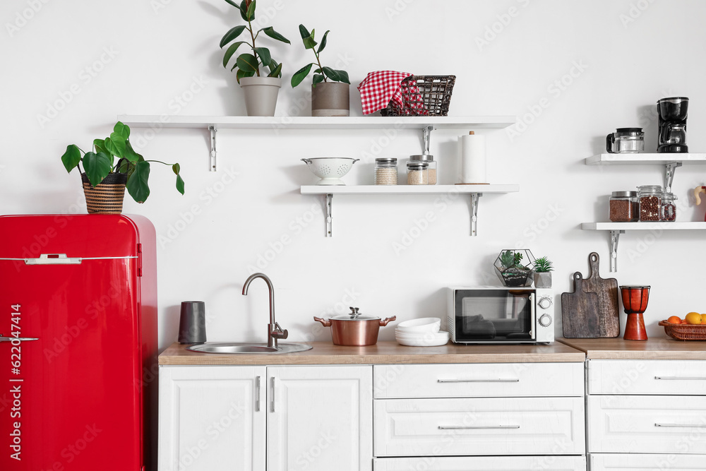 Interior of light kitchen with red fridge, counters, shelves and houseplants