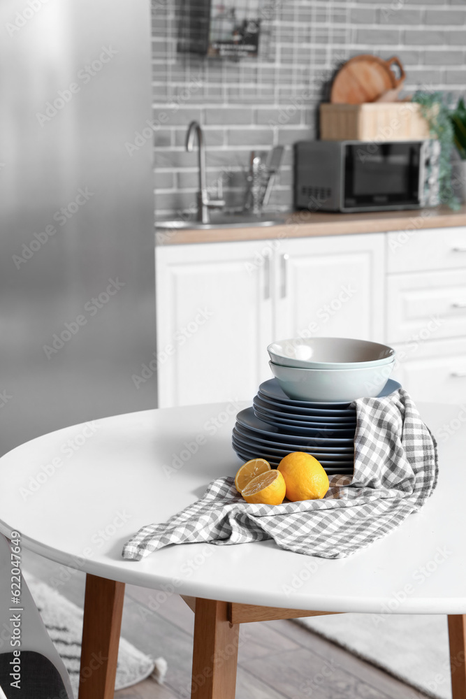 Table with lemons and plates in light kitchen, closeup