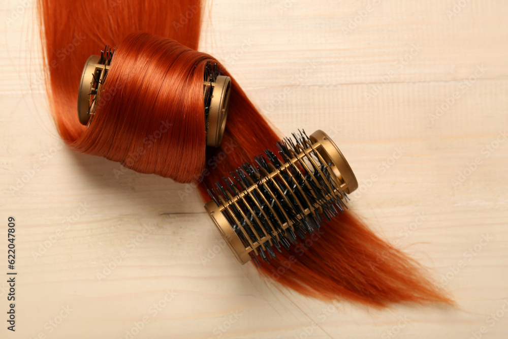 Ginger hair strand with curlers on light wooden background, closeup