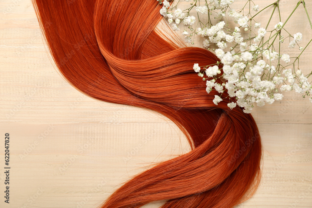 Ginger hair with beautiful gypsophila flowers on light wooden background, closeup