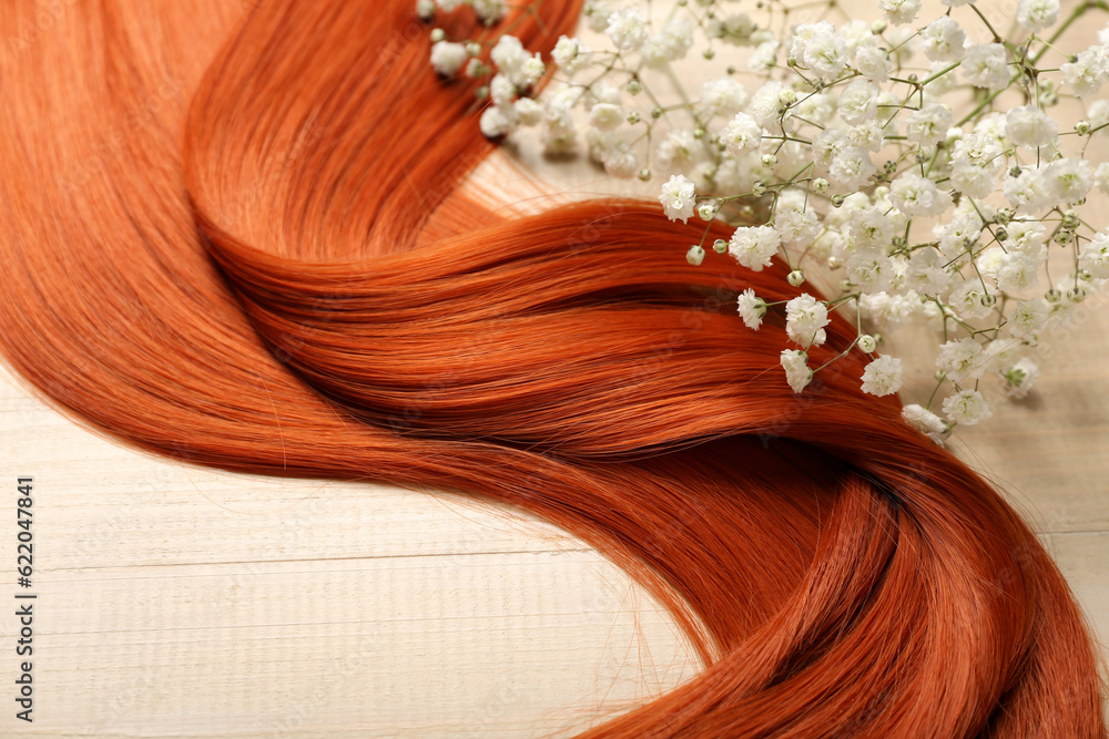 Ginger hair with beautiful gypsophila flowers on light wooden background, closeup